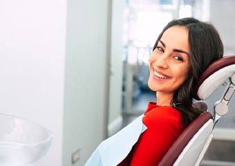 A woman wearing a red blouse and lying back in the dentist’s chair preparing for her appointment which she will pay for using dental insurance in Columbia
