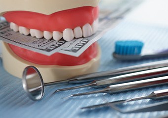 A jaw mockup biting hundred-dollar bills next to some dental tools