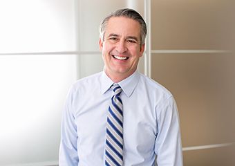 older man in blue dress shirt and tie smiling