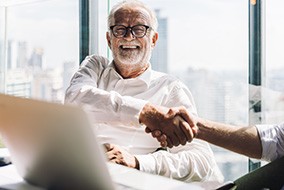 An older, smiling businessman shaking someone’s hand