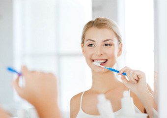 Blonde woman brushing her teeth in bathroom mirror