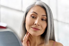 Older dental implant patient in Columbia looking at face in mirror