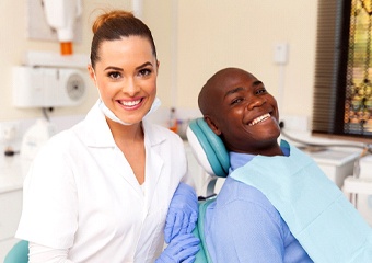 A male patient wearing a blue button-down shirt and smiling while his dental hygienist sits nearby and smiles