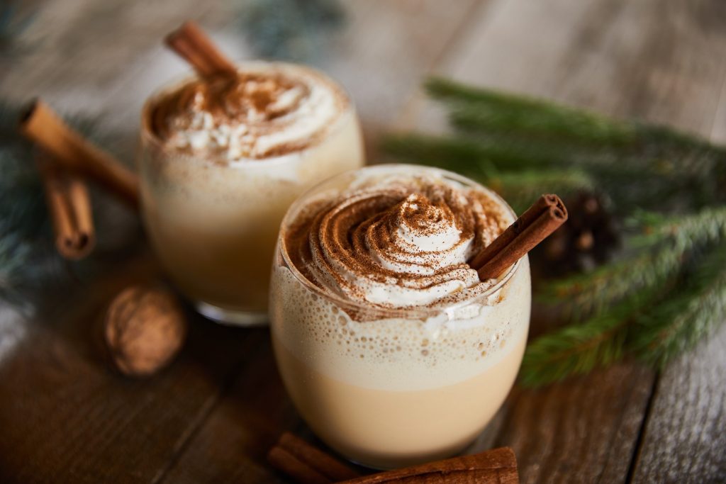Two glasses filled with eggnog and topped with cinnamon and a cinnamon stick