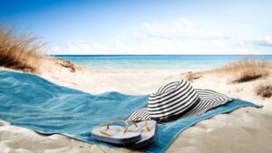 Blanket with hat and sandals spread out on the beach. 